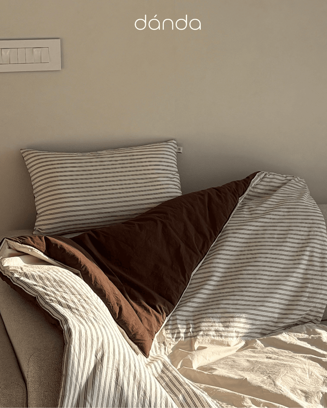 A minimalist home setting featuring a striped pillow and a draped blanket.